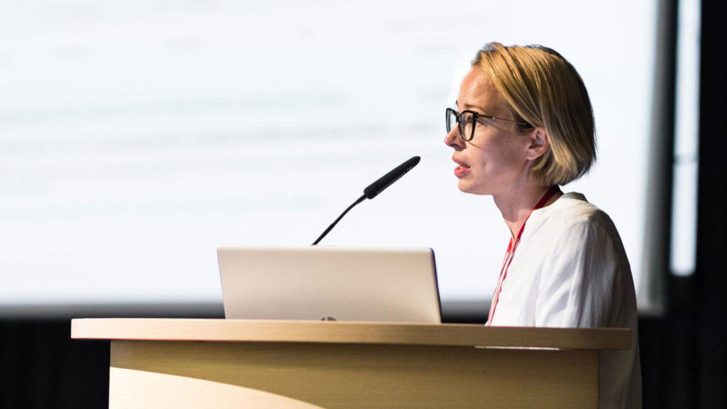 Female authoritative speaker at a lectern with a laptop